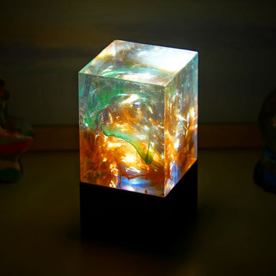 A cube-shaped decorative lamp with a desert hue, emitting a warm glow, placed on a flat surface.