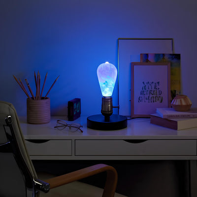 Colorful desk lamp on a desk with various items under blue lighting.